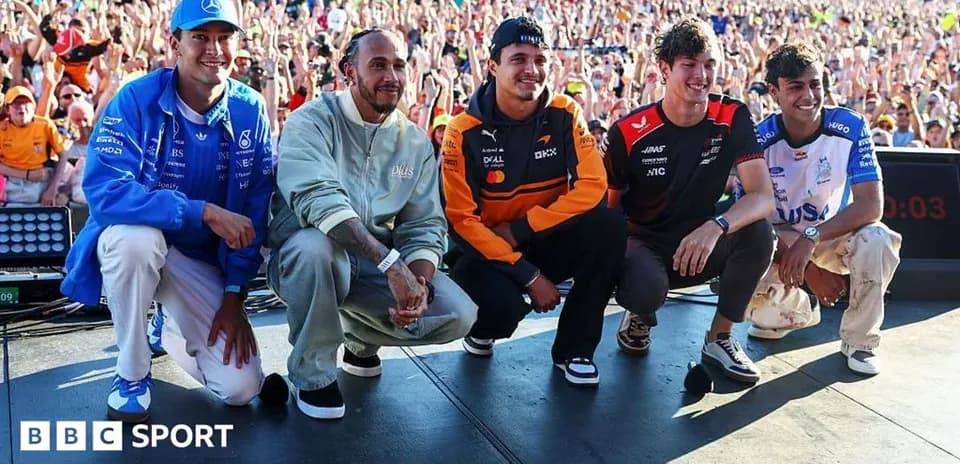 Formula 1 drivers posing on stage with crowd behind