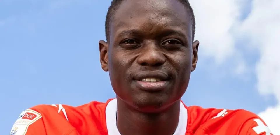 Futbolchi qizil forma kiyib, kamera tomonga qarab turibdi
