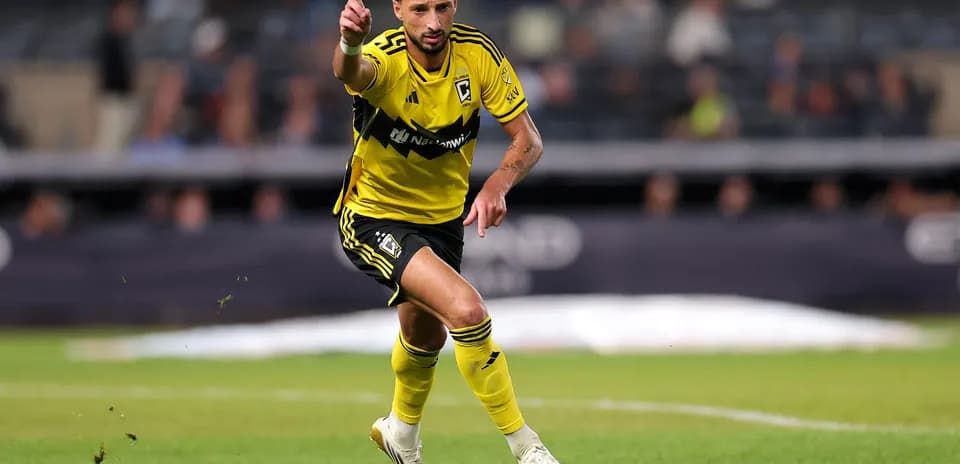 Futbolchi maydonda bir qo'lini ko'tarib yugurmoqda