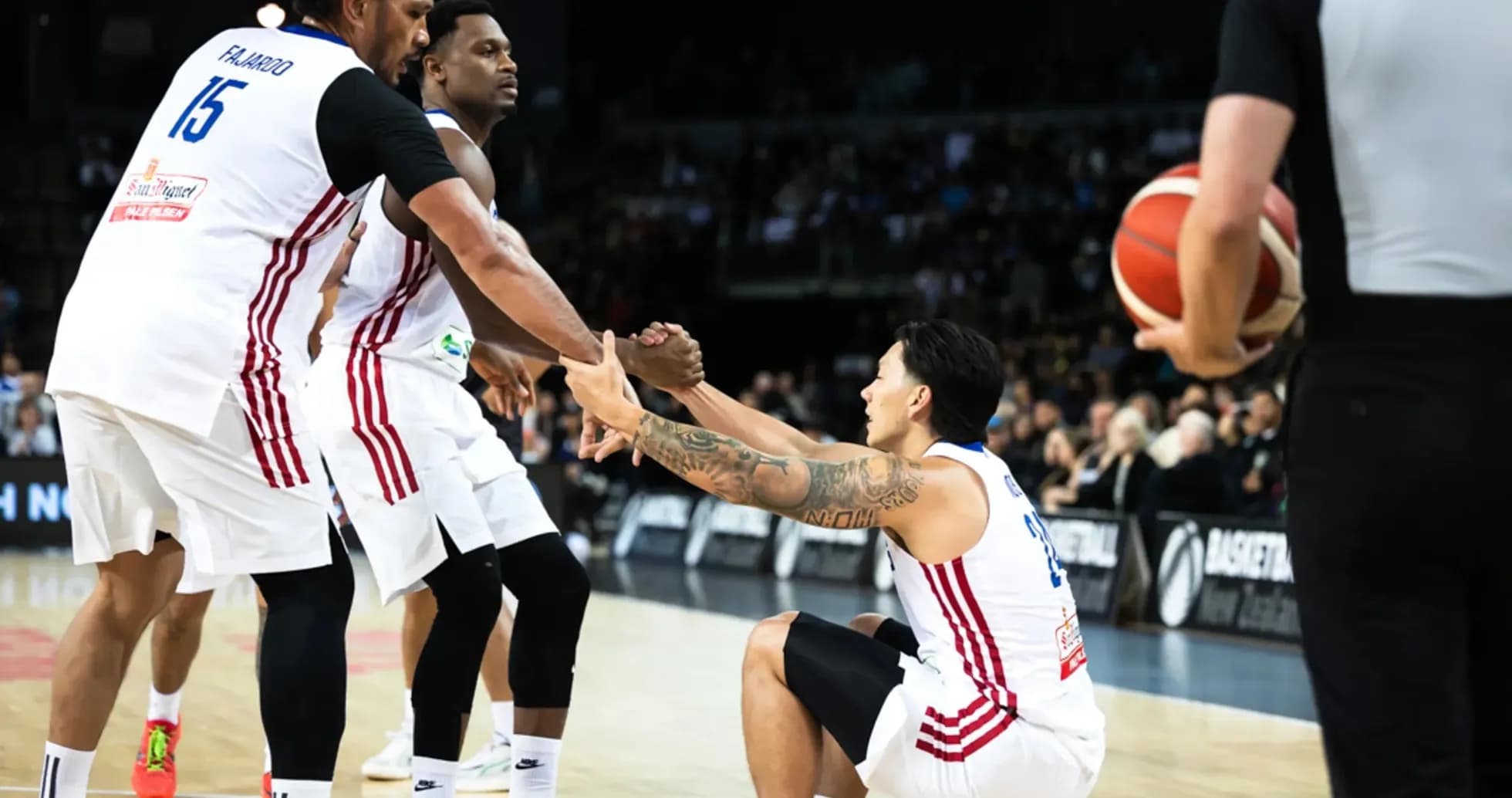 Two players helping teammate up from the court