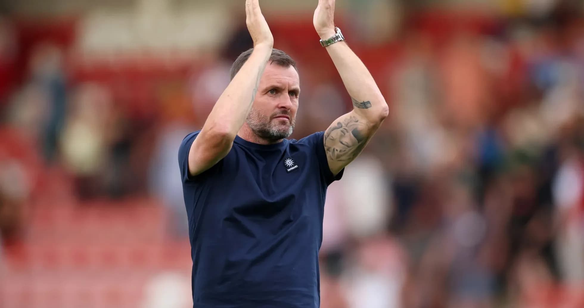 Men's football coach applauding fans after match