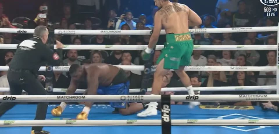 Boxer in green celebrating while opponent kneels down