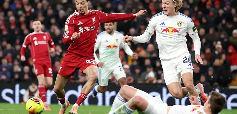 Liverpool player dribbling past Leeds opponents on pitch