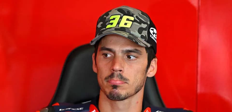 MotoGP rider seated with cap in paddock