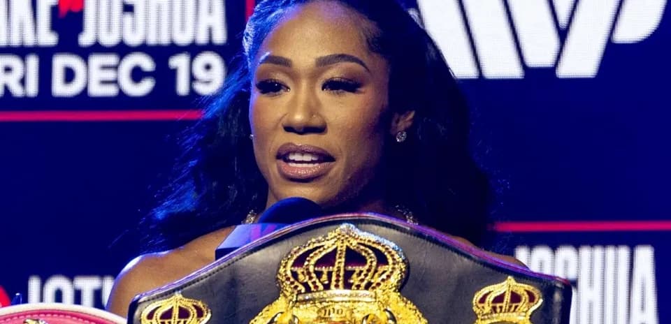 A woman speaking with boxing belts at podium