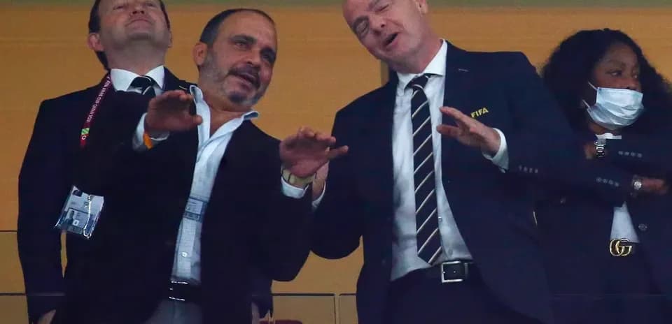 Two men in suits conversing in a stadium box