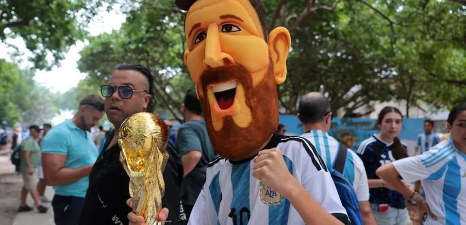 Fan wearing Messi mask holding World Cup trophy