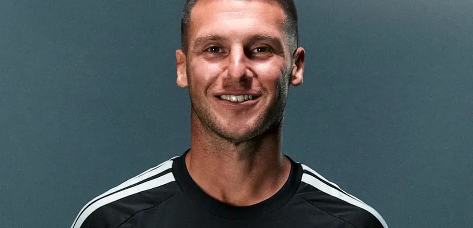 Futbolchi qora forma kiygan holda kulmoqda