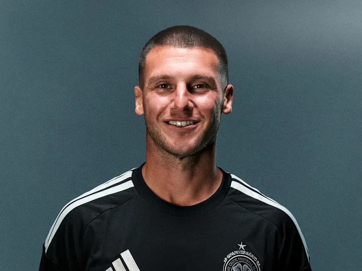 Futbolchi qora forma kiygan holda kulmoqda