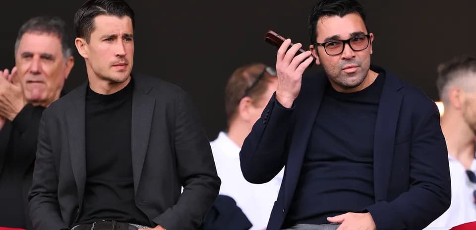Two men seated in stadium, one on phone