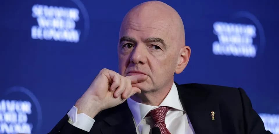 Man speaking at a conference with FIFA logo pin