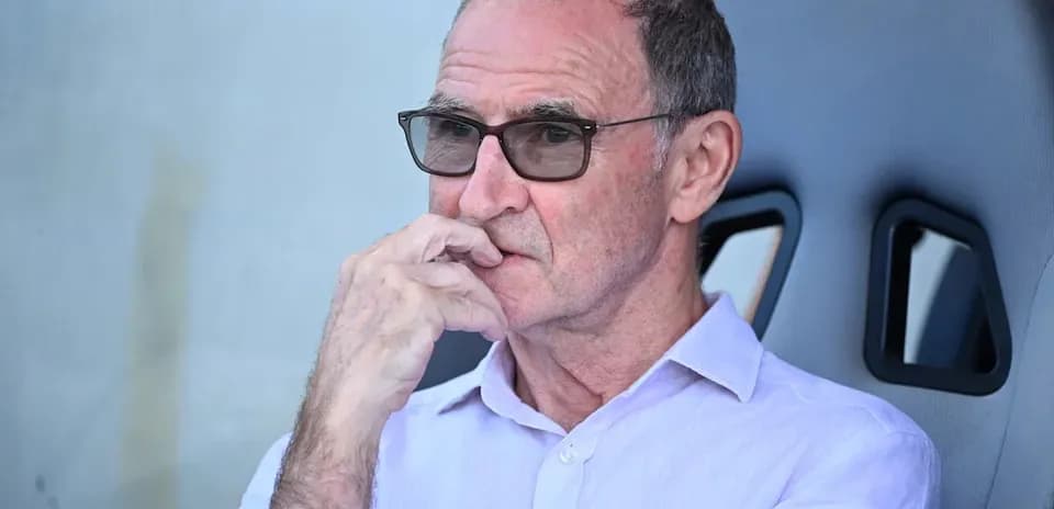 Person seated in dugout, wearing glasses and thinking