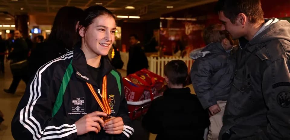Athlete displaying medal at airport with fans