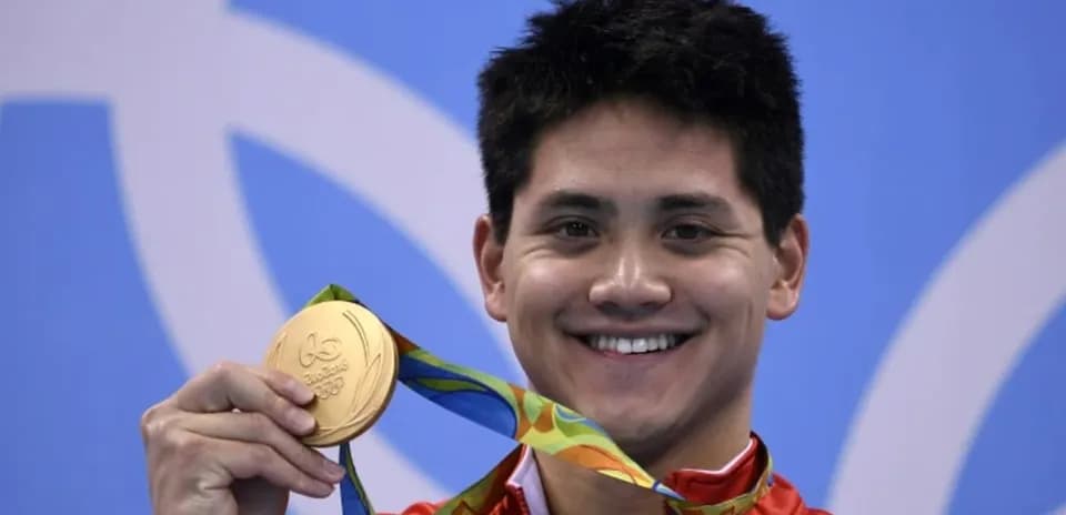 Sportchi oltin medalni ko'tarib turib tabassum qilmoqda