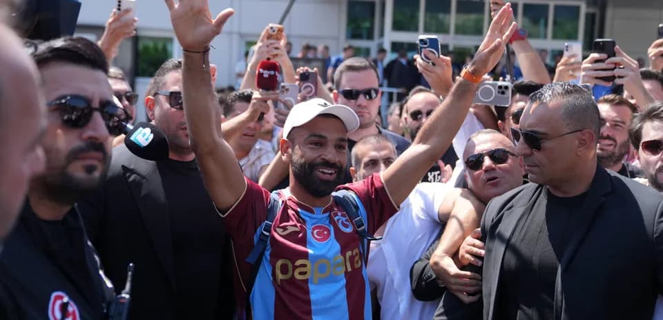 Futbolchi muxlislar orasida qo'l ko'tarib turibdi