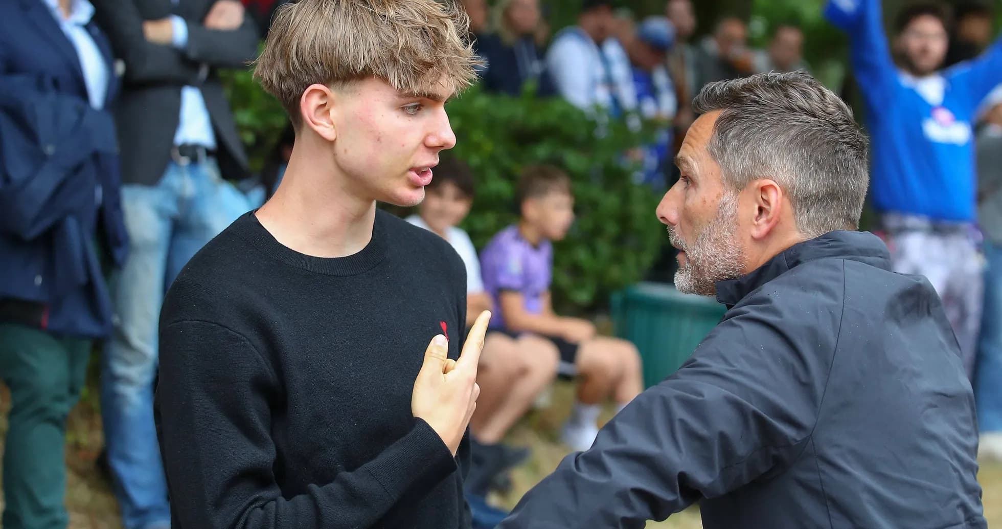 Young man speaking with adult in crowd