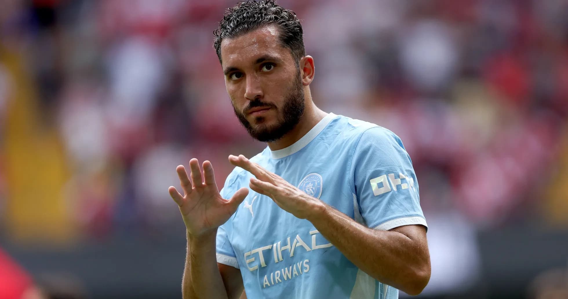 Futbolchi maydonda qo'lini ko'tarib turibdi