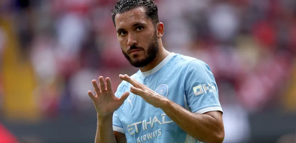 Futbolchi maydonda qo'lini ko'tarib turibdi
