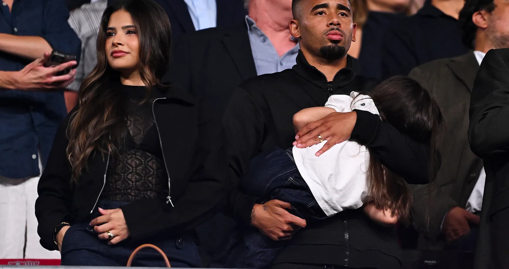 Couple with child at an event, spectators in background