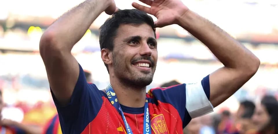 Futbolchi qizil forma kiygan, qo'llarini ko'tarib turibdi
