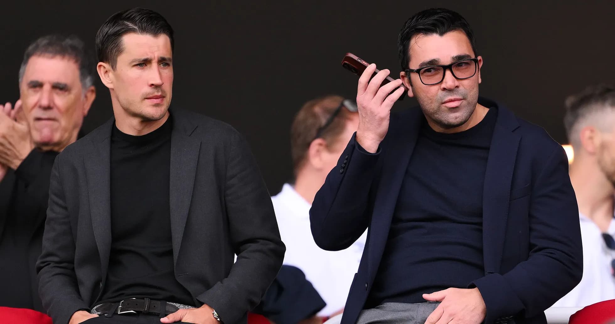 Two men seated in stadium, one on phone Two men seated in stadium, one on phone