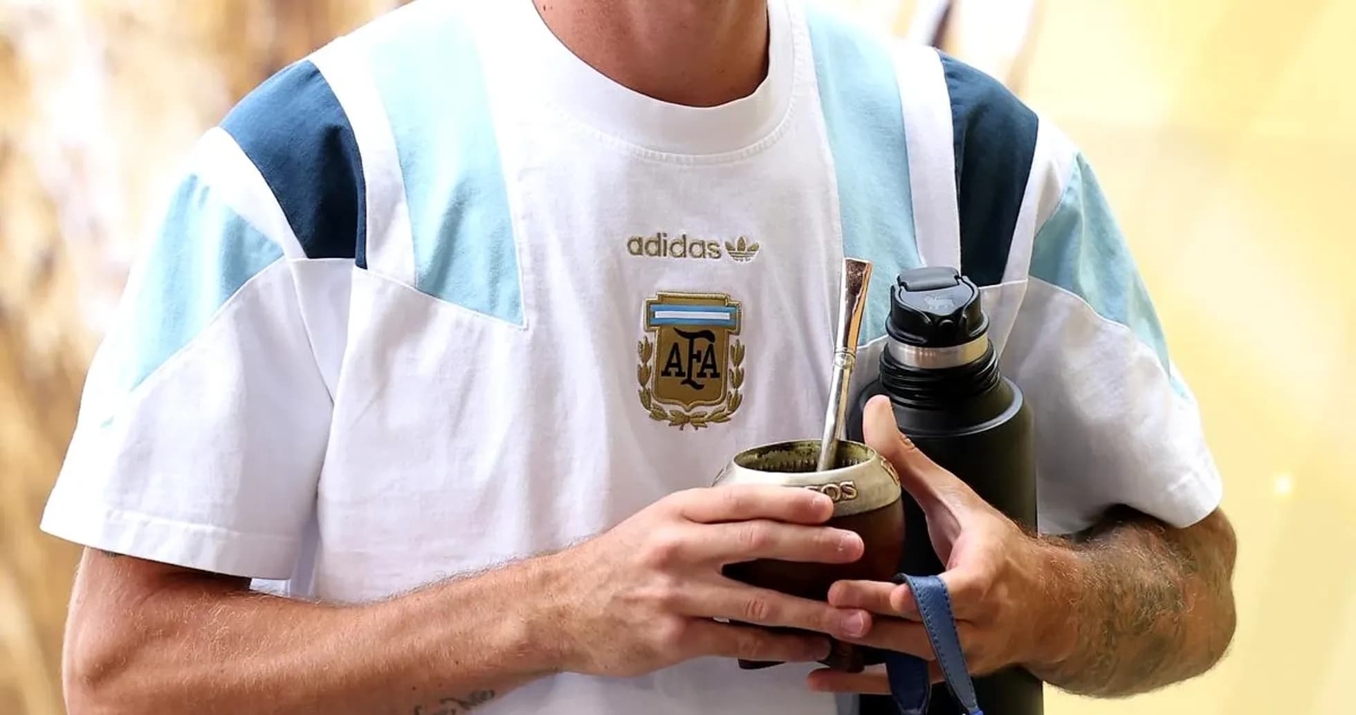 Futbolchi Argentina formasini kiyingan, ichimlik ushlab turibdi Futbolchi Argentina formasini kiyingan, ichimlik ushlab turibdi